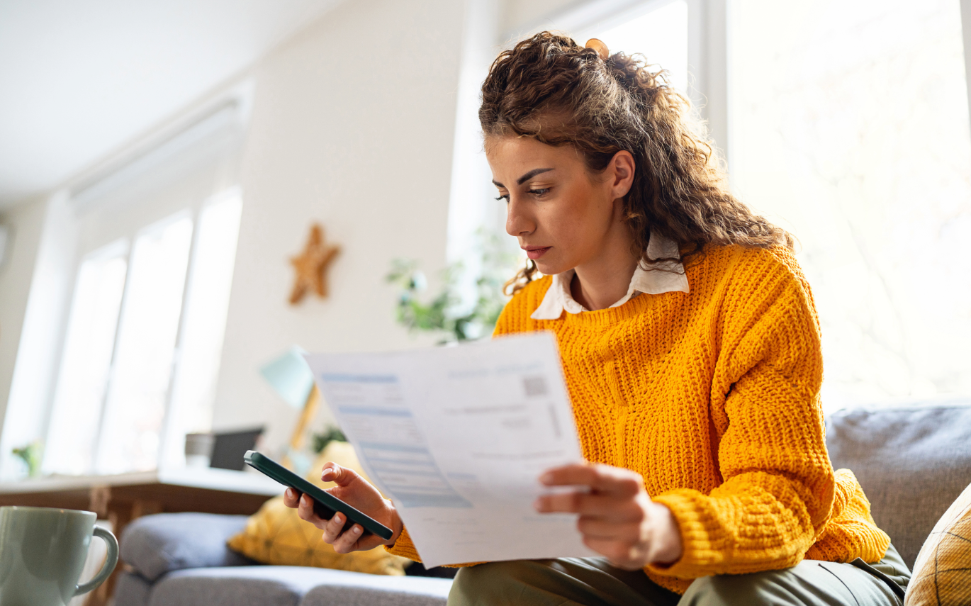 Woman sitting on couch at home looking at bills and phone