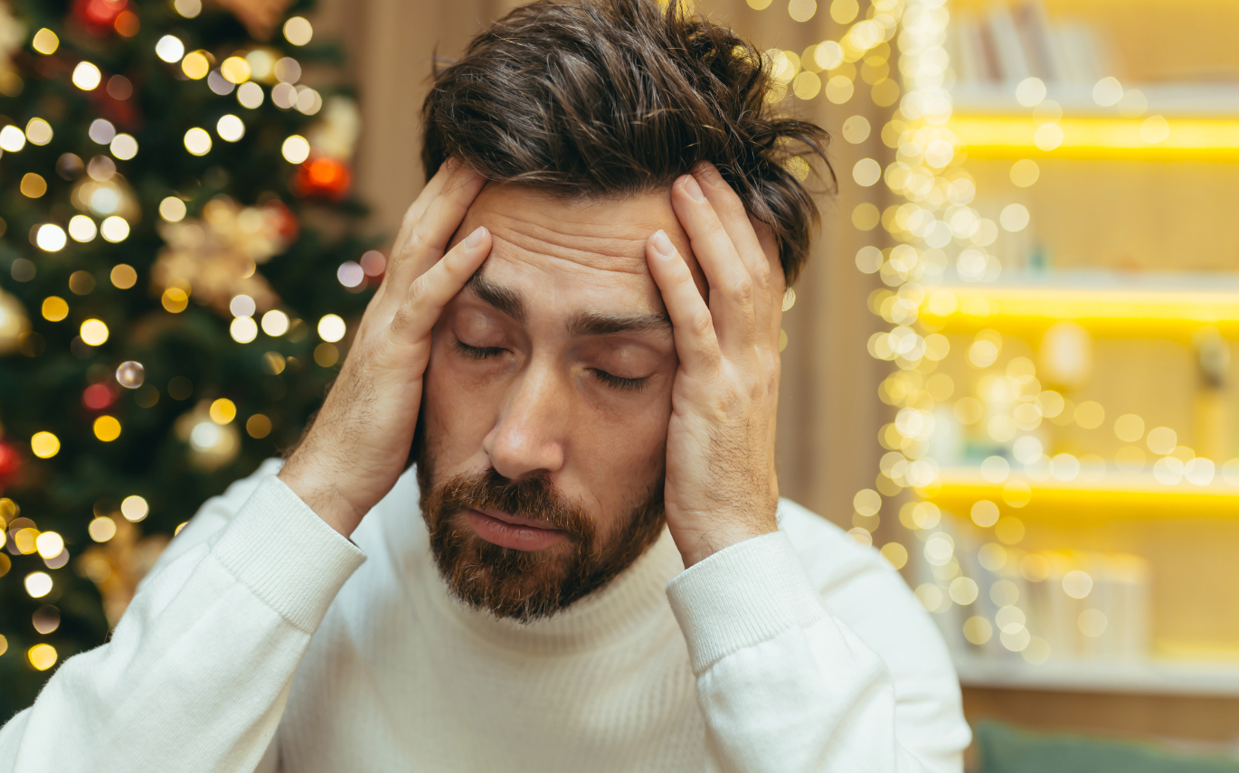 Stressed out man holding his head with holiday decorations in the background
