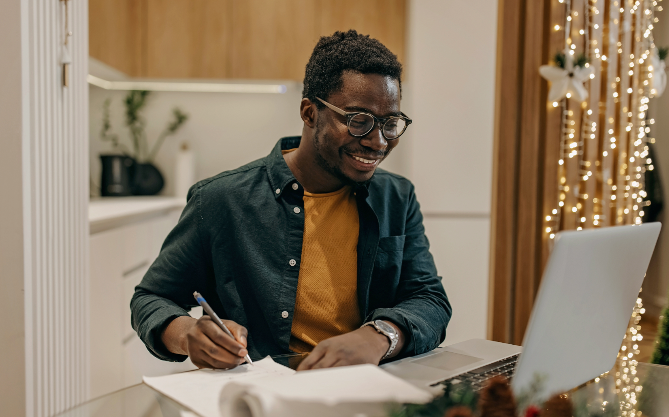 man using his computer and taking notes