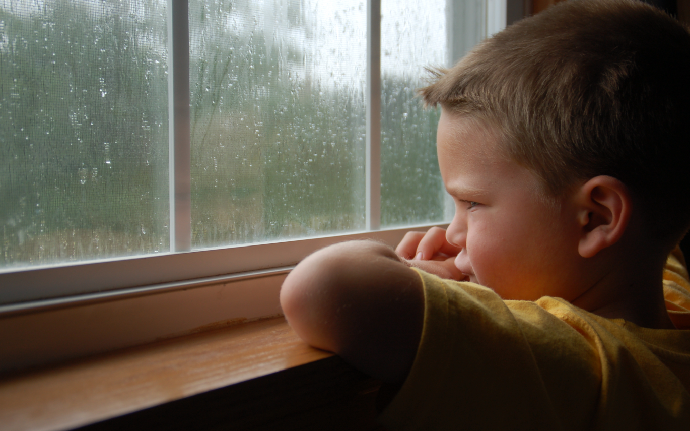 young boy looking out the window while it's raining