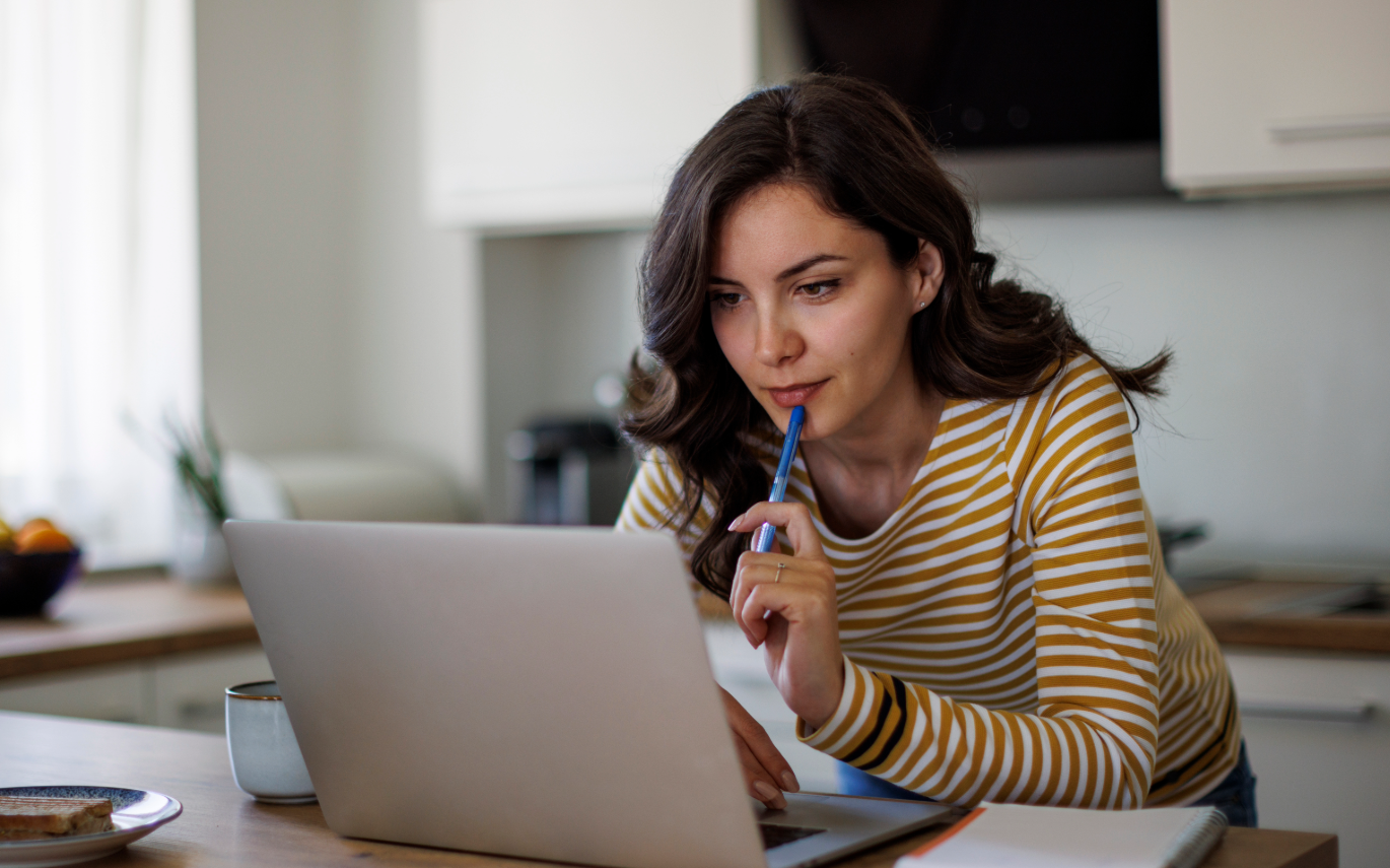 woman holding a pen and looking at her computer looking contemplative