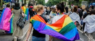 Two women walking in pride parade with pride flag