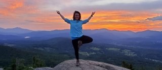 Yoga teacher doing a yoga pose on a mountain top in front of a sunset