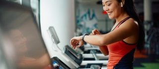 Athletic woman using fitness tracker while running on treadmill