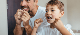 father and son flossing their teeth together in a mirror