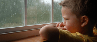 young boy looking out the window while it's raining