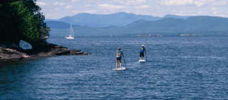 two people stand up paddle boarding with mountains in the background
