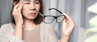 woman experiencing eye pain, holding her glasses