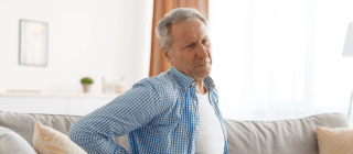 man sitting on couch experiencing lower back pain