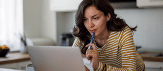 woman holding a pen and looking at her computer looking contemplative