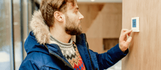 man adjusting thermostat in winter