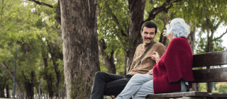 Young man and older woman sitting on a bench in a public space and chatting