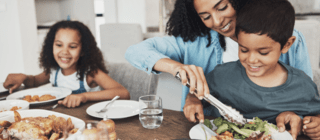 Mom serving a smiling child a healthy meal with another child smiling in the background