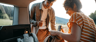 A couple packs their backpacks in the back of a car before a hike