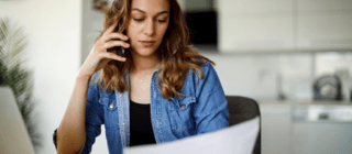 woman looking at a bill and laptop while on the phone