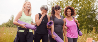 a group of four women walking together after a yoga exercise, holding mats and laughing and smiling
