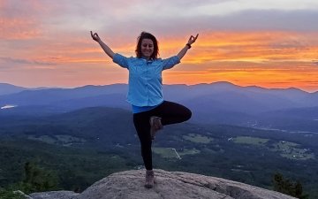 Yoga teacher doing a yoga pose on a mountain top in front of a sunset