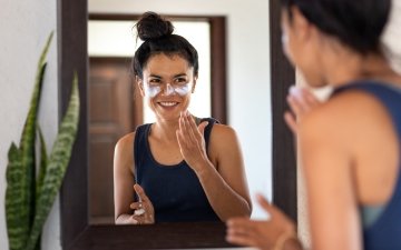 Woman applying white sunblock to face, looking at bathroom mirror, smiling