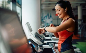 Athletic woman using fitness tracker while running on treadmill