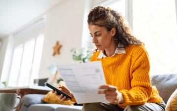 Woman sitting on couch at home looking at bills and phone