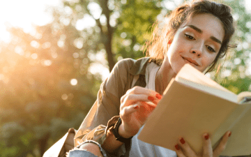 Woman reading a book outside surrounded by trees