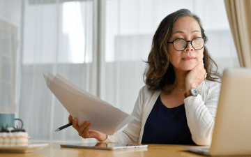 Woman holding papers, looking at laptop