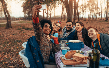 group of friends sharing a meal outside, taking a selfie