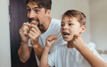 father and son flossing their teeth together in a mirror