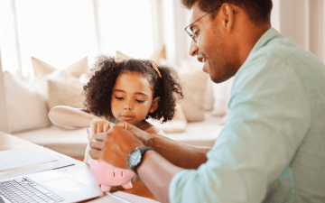dad talking to child about money with piggy bank