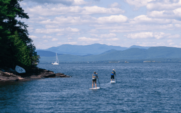 two people stand up paddle boarding with mountains in the background