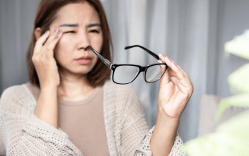 woman experiencing eye pain, holding her glasses