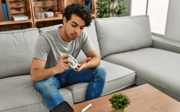 young man with diabetes sitting on a couch checking his blood sugar