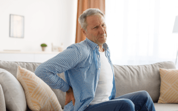 man sitting on couch experiencing lower back pain
