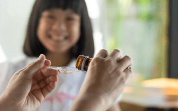 hands pouring a dose of medicine for a smiling child