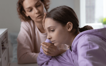 child looking upset with mother in the background