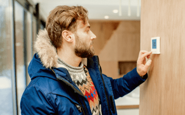 man adjusting thermostat in winter
