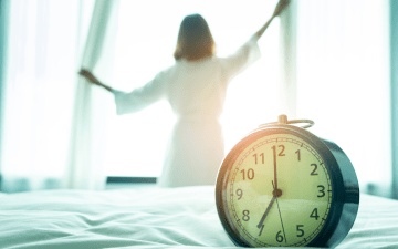 woman opening the curtains in her room with clock in the foreground