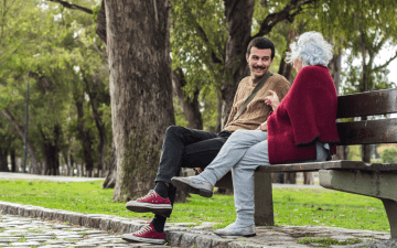 Young man and older woman sitting on a bench in a public space and chatting