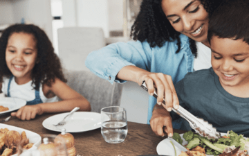 Mom serving a smiling child a healthy meal with another child smiling in the background