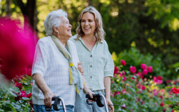 A woman walking with an older woman through a flower garden