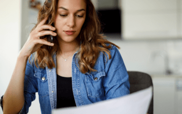 woman looking at a bill and laptop while on the phone