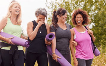 a group of four women walking together after a yoga exercise, holding mats and laughing and smiling
