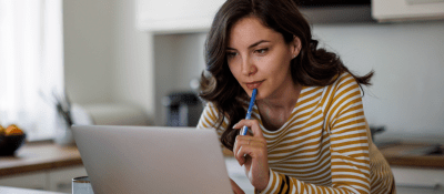 woman holding a pen and looking at her computer looking contemplative