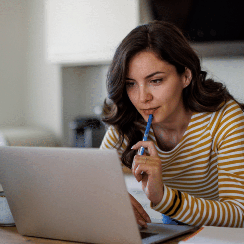 woman holding a pen and looking at her computer looking contemplative