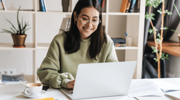 young woman looking at laptop with book shelf behind her