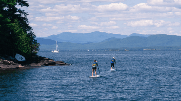two people stand up paddle boarding with mountains in the background