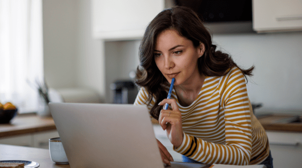 woman holding a pen and looking at her computer looking contemplative