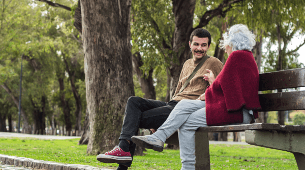 Young man and older woman sitting on a bench in a public space and chatting
