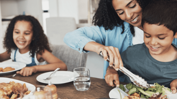 Mom serving a smiling child a healthy meal with another child smiling in the background