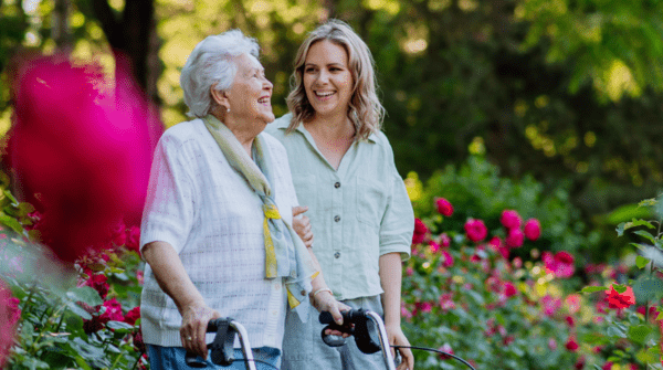 A woman walking with an older woman through a flower garden